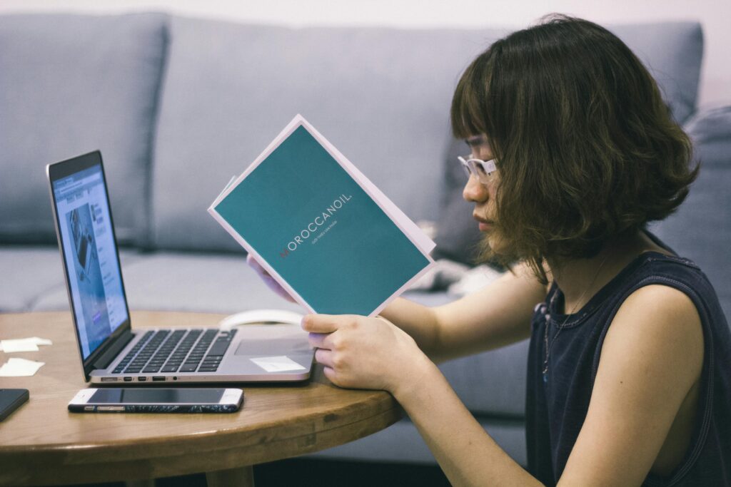 An Asian woman focuses on work with a laptop and document, creating a serene workspace scene.
